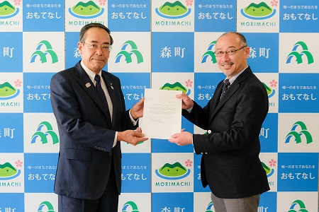 森町のバックボードの前で、眼鏡をかけたスーツ姿の男性2名が左右から答申書を持ち、笑顔で正面を向いている写真