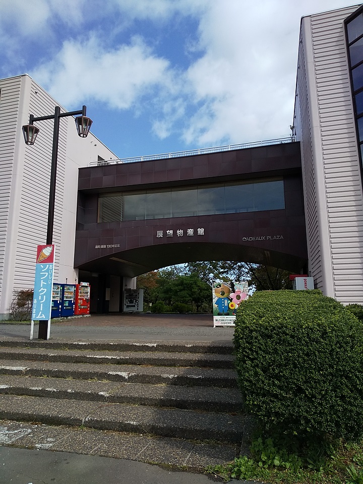 白い外壁の建物の間に設置された全面に大きな窓ガラスがある「展望物産館」と書かれた渡り廊下の写真