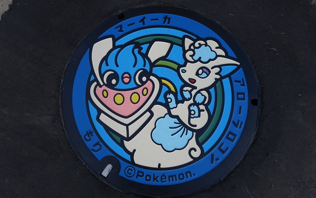 青色のふちに「マーイーカ」「アローラロコン」の文字とともに、白、青、ピンクの配色のイカ型のポケモンと、白、水色の配色のきつね型のポケモンが描かれたマンホールのふたの写真
